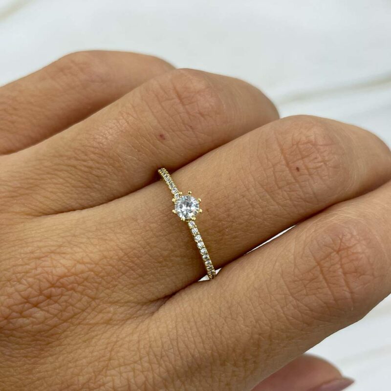 Anillo delgado de oro 18k con circones, modelo solitario, mostrado en mano femenina.