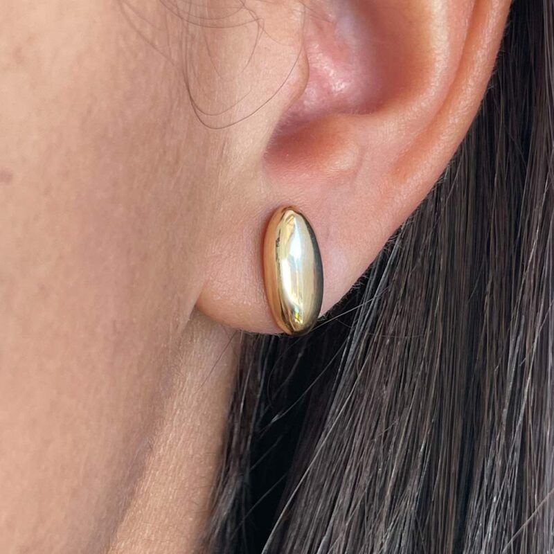 Aros pequeños ovalados de oro 18k para mujer, diseño liso y elegante usado en el lóbulo.