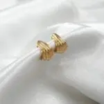 Aros pequeños de oro 18k con forma curva y acabado pulido, estilo elegante.